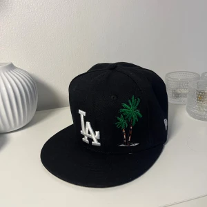 Svart LA Keps strl 55,8 - Svart LA Keps med palmträd som design. Strl 55,8