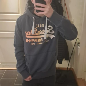 Superdry hoodie - Sjukt snygg superdry hoodie I blå färg med snygg orange-gul superdry logga. Tyvärr har tröjan ett håll I sig vid ena snöret men syns knapt när man har på sig den. Vid mer frågor kontakta mig✌️🍂