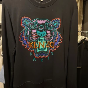 Svart Kenzo tröja med tigerbroderi - Svart tröja från Kenzo Tröjan har rund hals och långa ärmar. Broderiet har inslag av turkos, lila, orange och rött som gör den riktigt unik och sticker ut. Tröjan säljs inte längre och är svår att få tag i                                            Storlek: M Pris kan diskuteras vid snabbaffär