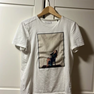 Vit t-shirt med print från Limitato - Vit t-shirt från Limitato med ett stort konstnärligt print framtill som föreställer en sittande kvinna. Klassisk passform och rund hals. Tillverkad i mjuk bomull för en skön känsla. Perfekt för dig som gillar unika motiv och stilrena plagg.