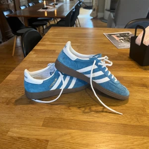 Adidas Spezial blå sneakers mocka - Säljer ett par Adidas Spezial sneakers i blå mocka med vita detaljer och klassiska tre ränder på sidorna. Skorna har vit hälkappa, vita skosnören och brun sula. Guldtexten 'Spezial' syns på sidan. Perfekta för dig som gillar retrostil och streetwear.