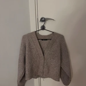 Beige kofta  - Säljer en beige ribbstickad kofta från Gina Tricot i storlek XS. Koftan har v-ringning, tre stora knappar framtill och långa ärmar. 