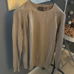 Beige tröja Oscar Jacobson - Snygg beige tröja från Oscar Jacobson, tillverkad i Italien. Tröjan har rund hals, ribbade muddar och lång ärm. Perfekt för dig som gillar stilrena och mjuka plagg med lyxig känsla. Passar dig som vill ha en klassisk look.