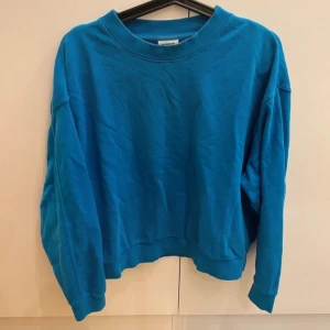 Blå sweatshirt  - En enkel och chill blå sweatshirt från Weekday med rund hals och långa ärmar. Tröjan har loose passform och är gjord i mjuk bomull, perfekt för att hänga med kompisar eller bara chilla hemma. Snygg att styla med jeans eller leggings.