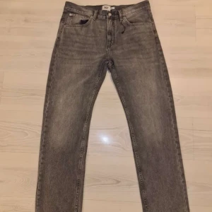 Grå jeans från 157, straight fit - Säljer ett par grå tvättade jeans från 157 med klassisk femficksdesign och raka ben. Jeansen har normal passform och är tillverkade i slitstarkt denimtyg. Perfekta för dig som gillar en enkel och stilren look.