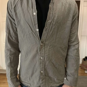 Två bomulls skjortor - Säljer två stilrena skjortor i bomull, en i grått/grönt och en i svart. Båda har lång ärm, knappar framtill. 