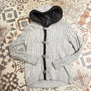 Grå stickad cardigan med teddyfoder🐻 - Säljer en grå stickad hoodie med mysig mörkgrå fleecefoder i huvan. Tröjan har ett snyggt kabelstickat mönster, fyra knappar framtill och ribbade muddar. Perfekt för dig som gillar chill och stil på samma gång. Storlek M.