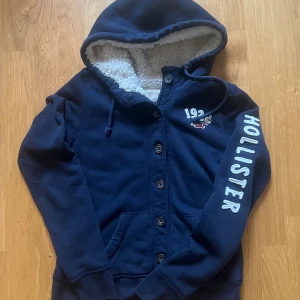 hoodie med knappar från Hollister - Säljer en marinblå hoodie från Hollister med fluffigt grått foder i hela tröjan. Tröjan har knappar framtill, Denna modellen är väldigt eftertraktad|.                                                             skriv vid funderingar.                                          Priset kan självklart diskuteras!