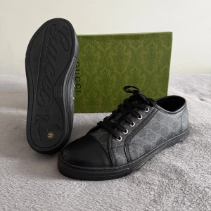 Gucci skor  - Snygga svarta sneakers från Gucci med klassiskt GG-monogram i grått på textilen och detaljer i svart skinn. Skorna har rund tå, svarta snören och platt sula. Perfekta för dig som vill ha en stilren och lyxig look med diskret logga.