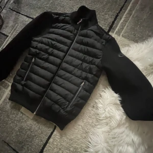 Svart pufferjacka från Moncler perfekt för höst-vinter🍂  - Säljer en svart pufferjacka från Moncler med quiltad front och släta ärmar. Jackan har dragkedja framtill, två fickor med dragkedja och Moncler-logga på ärmen. Perfekt för dig som vill ha en stilren och sportig look. passar storlekar S-M-L. Priset kan diskuteras.
