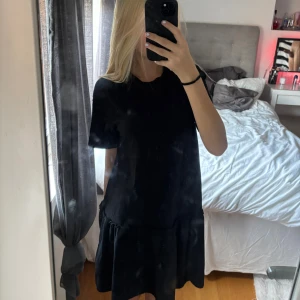 Svart kort klänning från 157 XS - Svart t-shirtklänning från 157 i storlek XS. Modellen är kort med rund hals, korta ärmar och en volangdetalj nedtill som ger en chill vibe. Tillverkad i mjuk bomull, perfekt för dig som gillar enkel och stilren look.