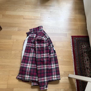 Rutig teddyjacka Tommy Hilfiger - Säljer en röd, vit och mörkblå rutig teddyjacka från Tommy Hilfiger. Jackan har mjukt teddyfoder, klassisk krage, knäppning framtill och stort Tommy Hilfiger-logga på ärmen. Perfekt för dig som vill ha en snygg och varm jacka för vintern.