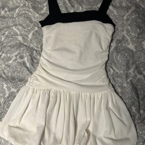 Vit och svart klänning Gina Tricot - Supersöt kort klänning från Gina Tricot i vitt med breda svarta axelband och överdel. Klänningen har en figurnära överdel och ett voluminöst, rynkat kjolparti. Perfekt för dig som gillar en stilren och trendig look.