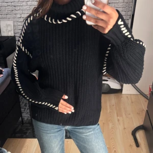 Polotröja  - Säljer en svart stickad polotröja med vita snörningsdetaljer längs kragen och ärmarna. Tröjan har grov ribbstickning och lång ärm och krage. Använd 1-3 gånger köpt på vero moda 