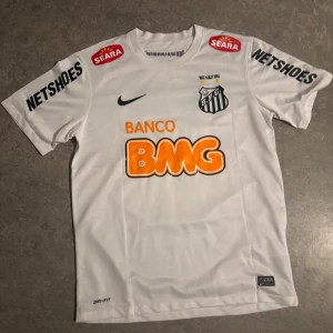 Santos Neymar Jr matchtröja Nike M - Säljer en officiell Santos FC fotbollströja med Neymar Jr och nummer 11 på ryggen. Tröjan är vit med svarta och orangea tryck, tillverkad i Nike Dri-Fit material för bästa komfort. Klassisk rund hals och korta ärmar, med flera sponsorer tryckta på både fram- och baksida.