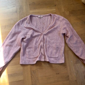 Ljusrosa kofta med v-ringning - Supermysig ljusrosa kofta från H&M med v-ringad hals och tre knappar framtill. Koftan har två praktiska fickor och är croppad i modellen. Perfekt att slänga på sig när det är lite kyligt ute.