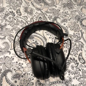 HyperX Cloud 1 Gaming Headset - HyperX Cloud II gaming headset med kabel och mikrofon. Over-ear design för komfort vid långa spelsessioner. Synligt slitage på huvudbandets läderimitation, men öronkuddarna är i bra skick. Perfekt för gaming med tydligt ljud och bra mikrofon.
