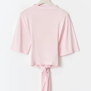 Ljusrosa omlottopp med knyt - Supersöt ljusrosa topp med omlottdetalj och knyt i ryggen. Toppen har korta ärmar och öppen rygg. Perfekt att styla med jeans eller kjol. Gjord i mjukt bomullsmaterial.