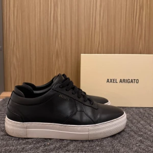 Axel Arigato Skor  - Svarta sneakers från Axel Arigato, Skorna är tillverkade i skinn och har snörning framtill. 