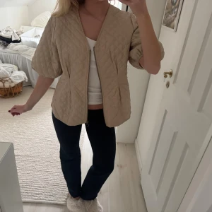 Beige/rosa quiltad jacka med puffärm - Quiltad beige/rosa jacka med puffiga trekvartsärmar och v-ringad hals. Jackan har dragkedja framtill och ett snyggt rutmönster över hela ytan. Perfekt för dig som gillar en chill och trendig look med lite volym i ärmarna. Jackan är från Lindex och i mycket bra skick!! Storlek L, men sitter som en M på mig som vanligtvis har S!!