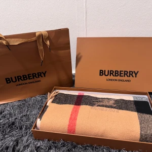 Burberry scarf - Exklusiv halsduk från Burberry i klassiskt rutigt mönster med beige, svart, vit och röd färg. Tillverkad i 100% kashmir och har broderad Burberry-logga samt ryttare. Kommer i originalförpackning och är mjuk och lyxig.