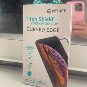 Skärmskydd för iPhone X/Xs/11 Pro - Helt ny Titan Shield skärmskydd i härdat glas för iPhone X, Xs och 11 Pro. 0,3 mm dubbelhärdat glas med kristallklar finish och böjda kanter. Skyddar mot repor, stötar och sprickor. Passar de flesta skal. Förpackningen är obruten och i mycket fint skick.