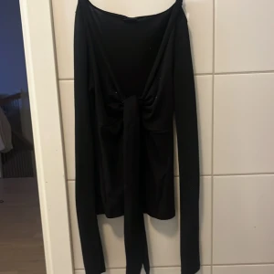 Svart långärmad omlottopp med knyt - Säljer en svart långärmad omlottopp från Gina tricot med snygg knytning framtill. Toppen har en djupare urringning och är gjord i mjukt, stretchigt material som sitter skönt mot kroppen. Perfekt för dig som gillar stilrena och trendiga plagg.