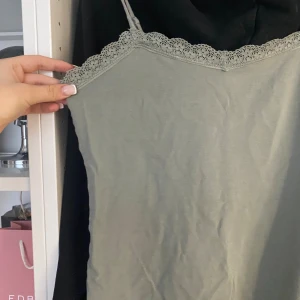Ljusgrön linnetopp med spetskant - Säljer en ljusgrön linnetopp med tunna axelband och dekorativ spetskant längs halsringningen. Toppen har en enkel och stilren design, perfekt för att skapa en chill och snygg look. Materialet känns mjukt och lätt mot huden.