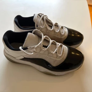 Nike Jordan 11 Low sneakers vit/svart - Säljer ett par Nike Jordan 11 Low sneakers i vit och svart med klassisk Jumpman-logga på plösen. Skorna har snörning, rund tå och en snygg kontrast mellan mesh och blankt syntetmaterial på ovandelen. Perfekt för dig som gillar streetwear och basketstil.
