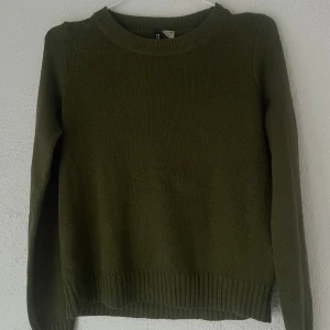 Olivgrön stickad tröja från H&M Divided - En enkel och snygg olivgrön stickad tröja från H&M Divided i storlek XS. Tröjan har rund halsringning, ribbade muddar och är långärmad. Perfekt att slänga på sig när det är kyligt ute.