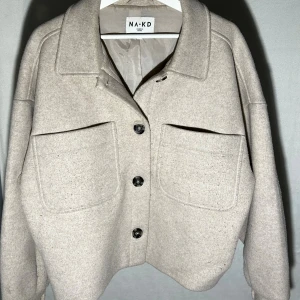 Beige jacka från NA-KD - Säljer en beige overshirt från NA-KD. Stilren och skön jacka!