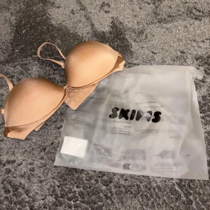 Beige push-up tubtopp från Skims - Säljer en beige push-up tubtopp från Skims med avtagbara axelband, aldrig använt då jag beställde fel storlek. Modellen är bandeau, materialet är mjukt och stretchigt. Perfekt när du vill ha axelbandslöst.💕💕