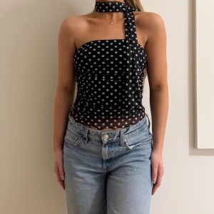 Svart prickig tubtopp med scarf - Säljer en svart tubtopp med vita prickar och matchande scarf runt halsen. Toppen är croppad och har en tight passform med transparent mesh nedtill. Perfekt för dig som gillar trendiga detaljer och ett lekfullt mönster.