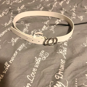 Vitt bälte med dubbelring-spänne - Snyggt vitt bälte med stilrent dubbelring-spänne i silverfärgad metall. Bältet har en slät yta och flera hål för justering. Perfekt accessoar för att lyfta din outfit med en clean och modern look. Finns ett hål som jag gjorde själv för att den var lite för stor för mig.
