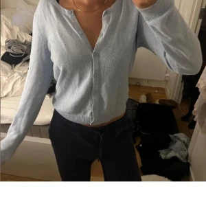 Ljusblå kofta med knappar - Snygg ljusblå kofta med långa ärmar och rund hals. Tröjan har en croppad passform och stängs med knappar framtill. Perfekt att slänga på sig när du vill ha en chill och stilren look. Materialet känns mjukt och lätt, passar bra till jeans eller kjol.