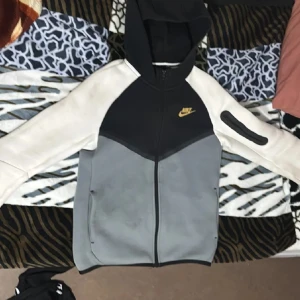 Nike hoodie jacka med dragkedja - Skicka till mig om ni vill ha mer bilder Nike jacka med huva i svart, grått och vitt. Jackan har hel dragkedja framtill, fickor på sidorna och en extra ficka med dragkedja på ärmen. Guldigt Nike-märke på bröstet. Perfekt för en sportig och avslappnad stil.