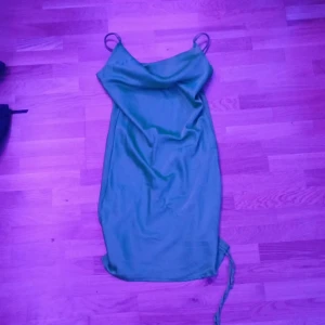 Grön satinklänning från Amisu - Snygg grön satinklänning från Amisu med smala axelband och draperad halsringning. Klänningen slutar lite över knänen på mig som är 176 cm. Den har justerbar längd med snöret på vänstra sidan.