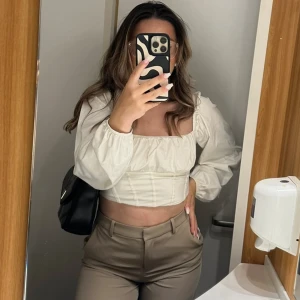 Vit croppad korsettopp med puffärm - Säljer en vit croppad korsettopp med långa puffärmar och fyrkantig halsringning. Toppen har markerade sömmar framtill som ger en snygg siluett och är tillverkad i ett lätt, vävt material. Perfekt för dig som gillar trendiga och feminina plagg. Ny pris 359kr från Gina Tricot. 