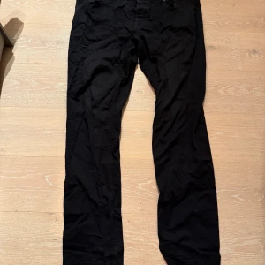 Svarta chinos från Benetton, stl 56 - Svarta chinos från United Colors of Benetton i storlek 56. Klassisk rak passform med fem fickor och knappgylf. Tillverkade i bomull för en skön känsla och stilren look. Perfekta för dig som gillar enkel och clean stil.