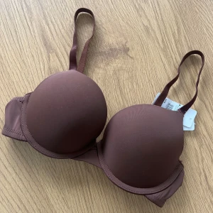 Ny BH <3 - Snygg push up-bh i chokladbrunt från cubus. Bh:n har justerbara axelband och vadderade kupor för extra lyft. Slät design utan mönster och klassisk hyskknäppning bak. Perfekt för dig som vill ha en stilren och bekväm bh i en trendig brun nyans.