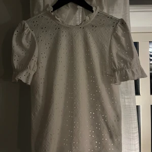 Vit blus med broderade detaljer - Säljer en söt vit blus med puffärmar och broderade hålmönster. Blusen har rund hals med liten volangkant och korta ärmar med resår. 