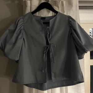 Blå blus med puffärmar och knyt - Säljer en ljusblå blus från Gina Tricot med puffiga korta ärmar och två snygga knyt framtill. Blusen har en rund halsringning och är tillverkad i ett mjukt bomullsmaterial. 