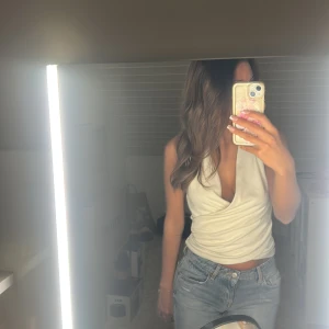 Vit omlott linnetopp med v-ringning - Säljer en snygg vit omlott linnetopp med djup v-ringning och croppad passform. Toppen är ärmlös och har en stilren, modern look som passar perfekt till jeans eller kjol. Materialet känns mjukt och lätt mot huden. Perfekt för dig som gillar trendiga och fräscha outfits.