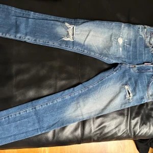 Blå Dsquared2 jeans  - Snygga blå jeans från Dsquared2 med hål och slitningar i fram och  stor svart Dsquared2-logga över fickorna. 