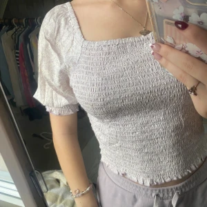 Ljuslila blus med puffärm från KappAhl - Supersöt ljuslila blus från KappAhl med smockad kropp och puffiga kortärmar. Blusen har små broderade hålmönster på ärmarna och en fyrkantig ringning. Finns matchande kjol!!