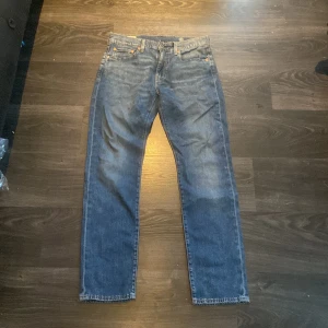 Levi's Premium blå jeans straight fit - Snygga Levi's Premium jeans i klassisk blå tvätt med raka ben och fem fickor. Jeansen har orangea sömmar, läderpatch bak och den ikoniska röda Levi's-taggen. Perfekt passform med normal midja och tillverkade i slitstarkt bomullsjeansmaterial.