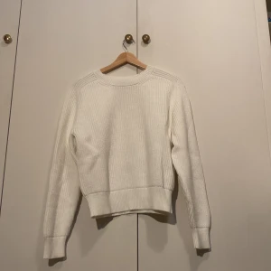 Vit stickad tröja med rund hals - En stilren vit stickad tröja med rund halsringning och ribbade muddar. Tröjan har en klassisk passform och är perfekt för lager-på-lager. Långärmad och enkel att matcha med jeans eller kjol.