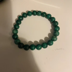 Grönt pärlarmband med stenkulor - Snyggt armband med runda gröna pärlor av sten. Perfekt för dig som gillar enkel och stilren design med naturliga material. Elastiskt band gör det lätt att ta på och av. Passar till många olika outfits och ger en cool touch.