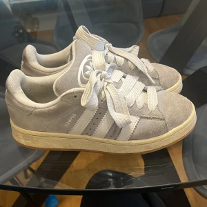 Grå Adidas Campus sneakers - Säljer ett par grå Adidas Campus sneakers med klassiska vita ränder på sidorna och vit snörning. Bra skick och använts ungefär 1 månad.  Köparen står för frakten! 
