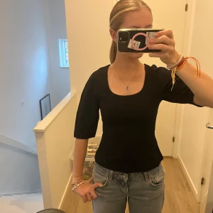 Svart topp Gina Tricot - Snygg svart topp från Gina Tricot i storlek XS. Modellen har en fyrkantig halsringning och halvlånga ärmar. Toppen är figurnära och gjord i mjuk bomullsmix som sitter skönt mot kroppen. Perfekt att styla med jeans eller kjol för en clean look.